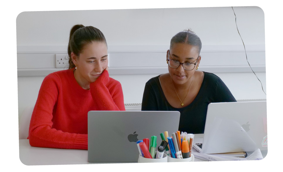 Bethy and Monai sat on laptops working together on the behaviour change challenge.