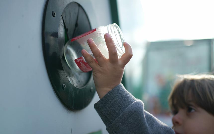 A young boy places a glass jar into the glass deposit box.