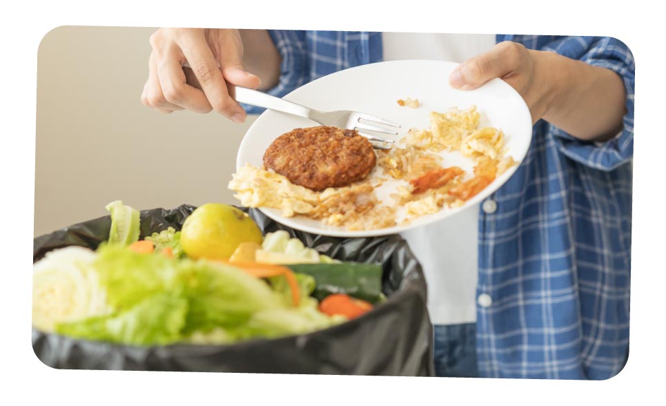 A person scraping un-eaten food into a waste bin.