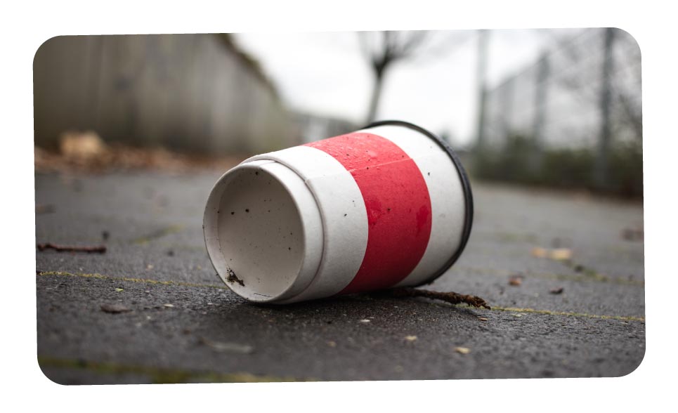 A dirty white and red disposable coffee cup on the ground.