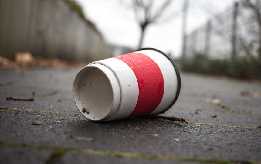 A dirty white and red disposable coffee cup on the ground.