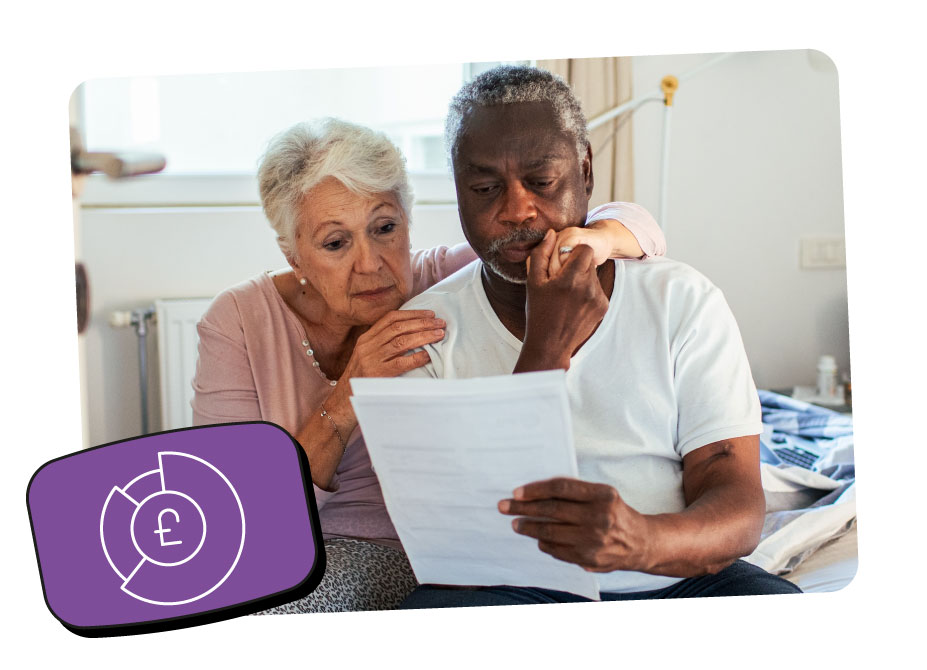 Two seniors sit closely on a bed in a softly lit room while looking thoughtfully at a document.