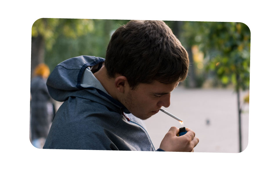 A close-up of a man lights up a cigarette in a public park.