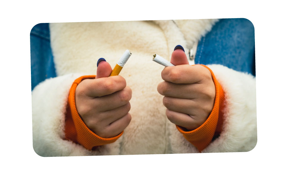 A close-up of a girl's hands in a fluffy coat as she snaps a cigarette in half.