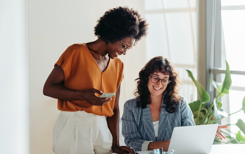 Two women smiling in an office looking at a laptop