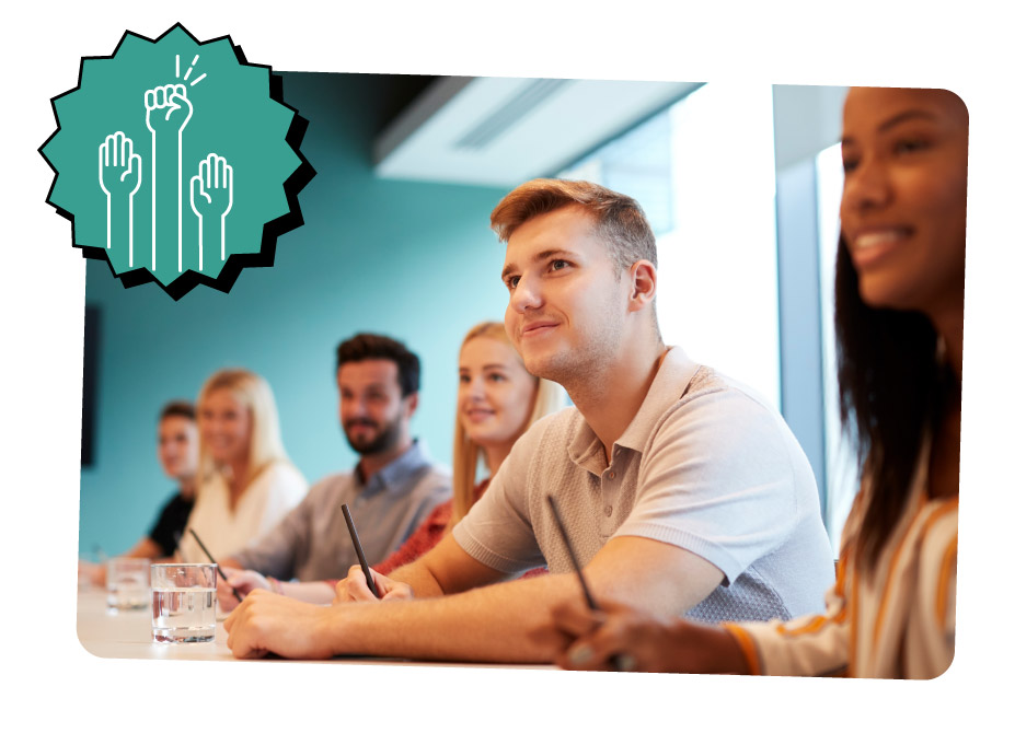 A group of people sitting at a conference table in a modern meeting room, attentively listening and taking notes.