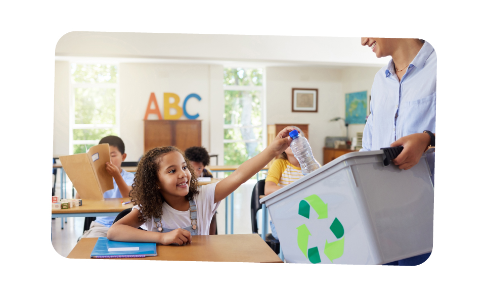 Child putting plastic bottle into recycling bin sat in classroom