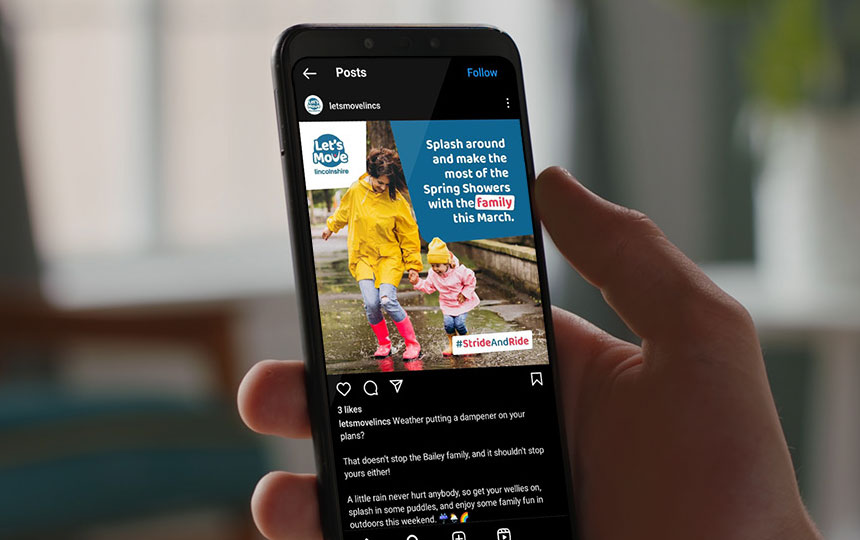 A close-up photo of a person holding their smartphone which displays a branded design for a social media post.