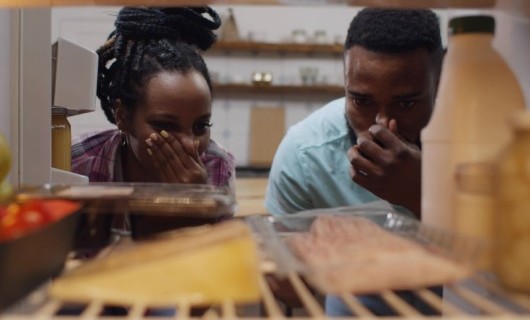 Two people looking inside their fridge and holding their noses to block the smell of expired food.