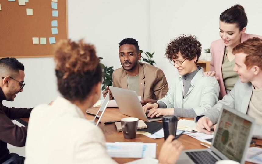 A group of professionals are having a meeting around a table with laptops, mugs and notebooks.