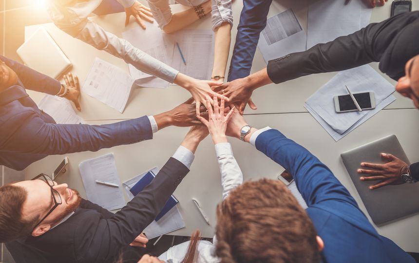 Eight people each put a hand into the middle of a table, one on top of another.