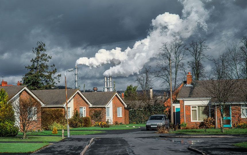 Bungalows in an English suburb with large factories emitting pollution in the background.