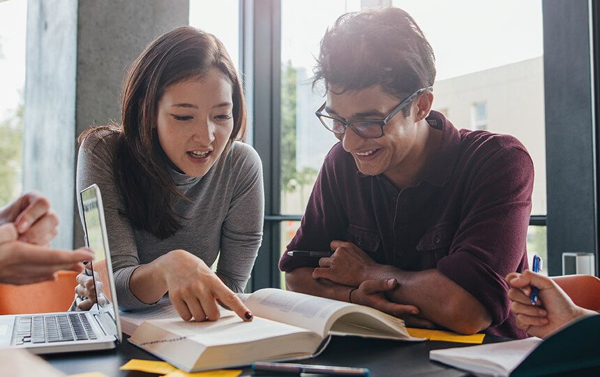 Two students read together from a book as one points to a part of the page.