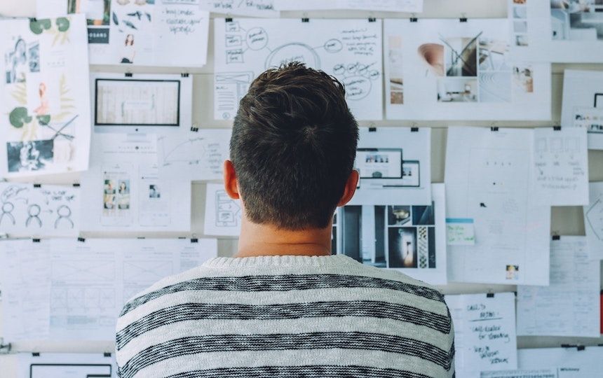 Seen from behind, a man is staring at a noticeboard full of images, graphs and diagrams.