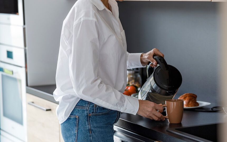 A woman is making a cup of tea in her kitchen.