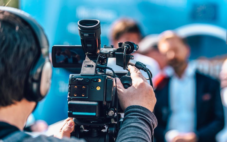A camera operator films an out of focus scene of two men talking directly to the camera.