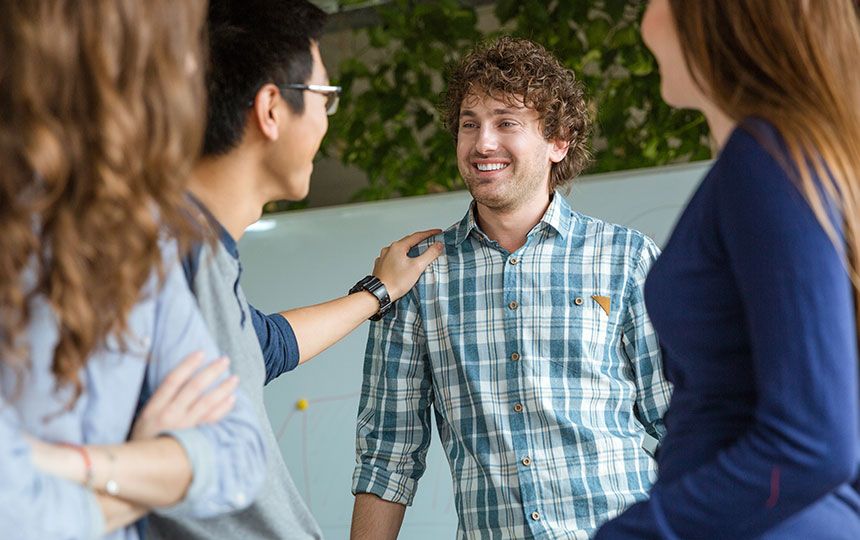 A man in a checked blue shirt is smiling while his friend puts his hand on his right shoulder.