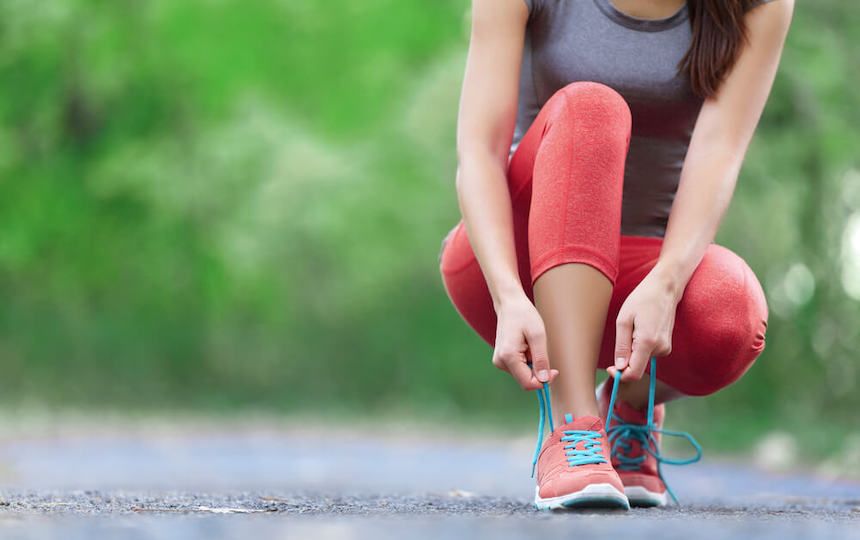 A woman on a path bending down to tying her trainers during a running or walking session.