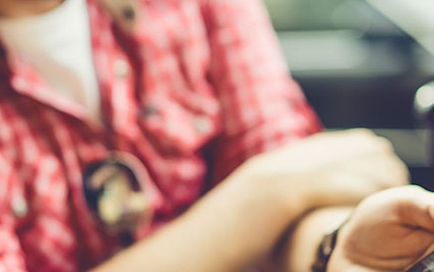 A blurred image of a man sat in the car, holding his phone out to share what's on the screen.