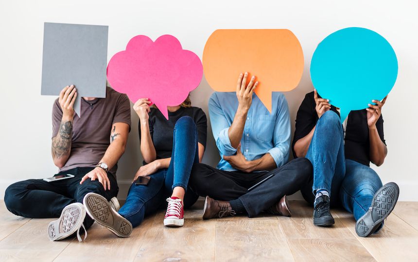 Four people are sat holding different shaped speech bubbles in front of their faces.