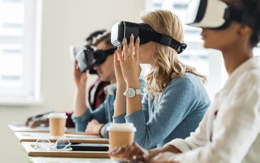Four people are sat in a row, at separate desks and are wearing virtual reality headsets.