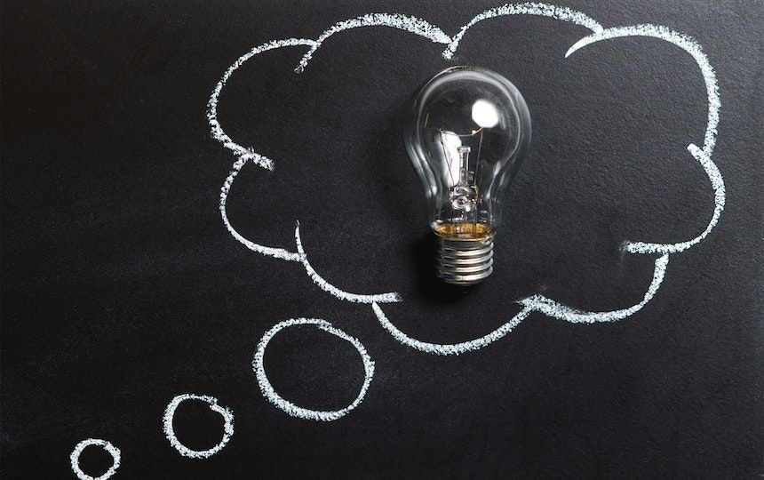 A black chalkboard has a thought bubble drawn out in white chalk, with a lightbulb in the middle.
