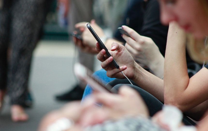 A group of people are sat down in a row looking at and using their smartphones.