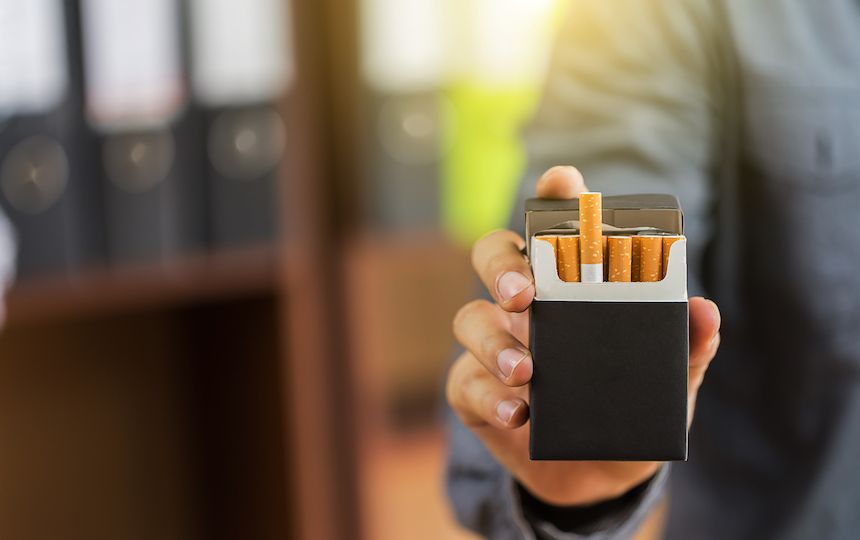 A man's hand holding a black packet of cigarettes, with one cigarette raised in the packet.