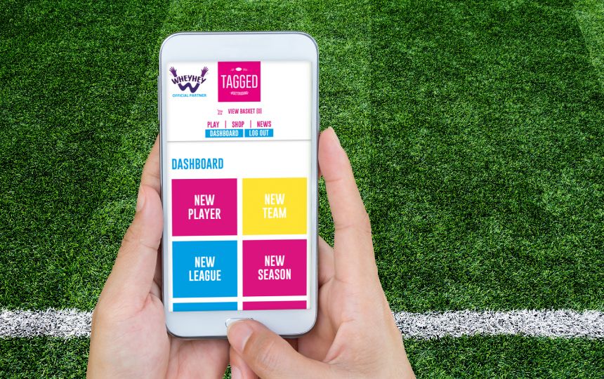 Someone holds a phone in front of a green astroturf back drop, which displays the Tagged website.