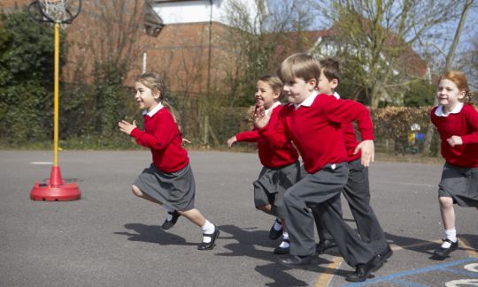A group of school children in red jumpers running across the school