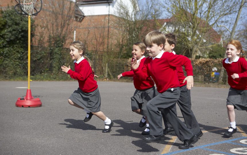 A group of school children in red jumpers running across the school's playground.