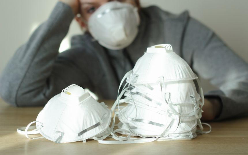 Someone wearing a face mask holds their head, staring at a pile of facemasks.