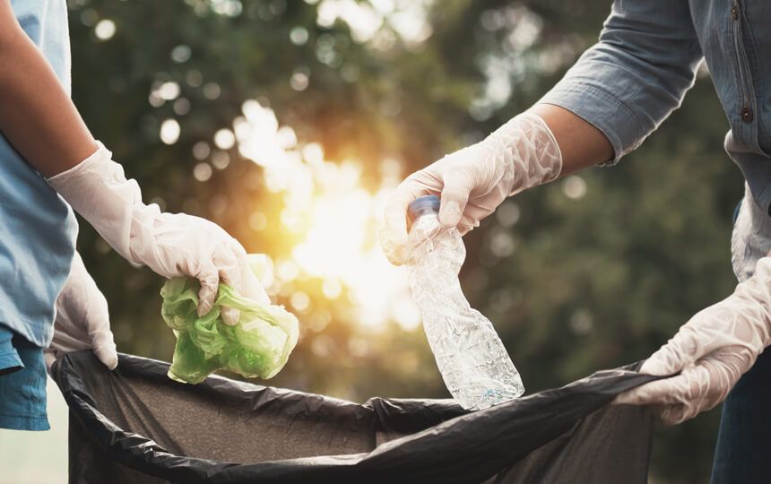 2 people hold a refuse sack open as they throw in plastic waste.