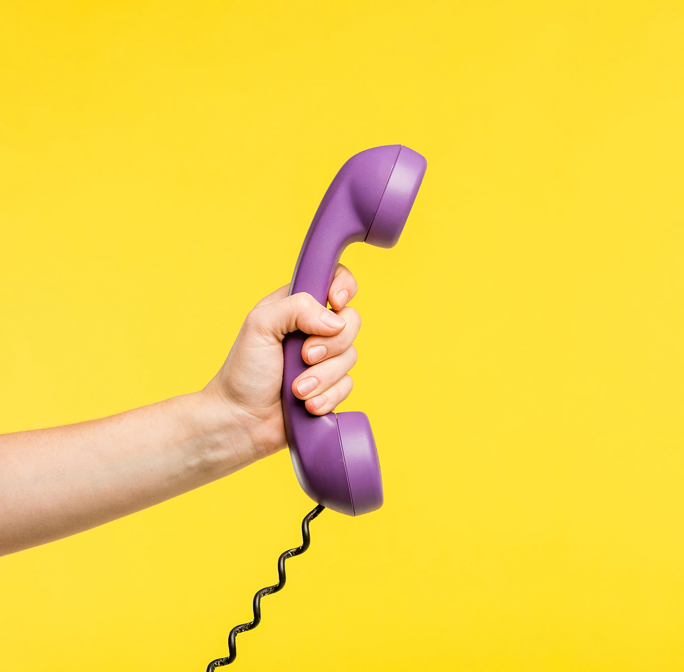 A hand holding a purple retro phone against a bright yellow backdrop.