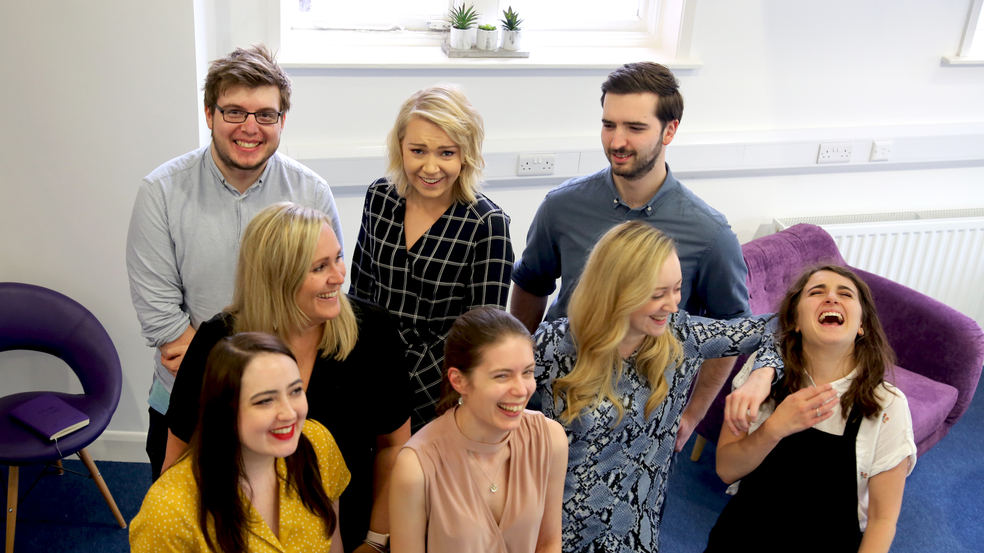 The Social Change UK team stand in a group laughing at each other, in the Social Change UK office.