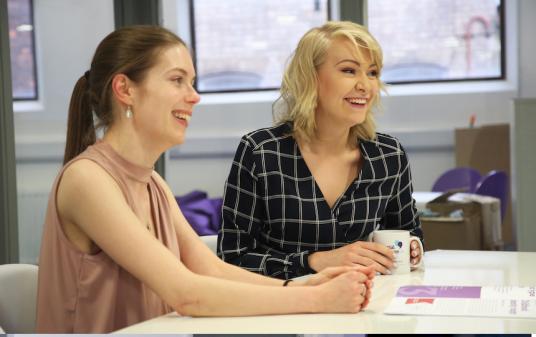 Chloe and Eloise sit in the Social Change UK meeting room, drinking tea and laughing.