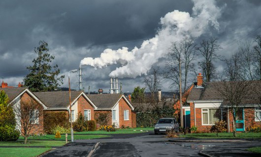 Bungalows in an English suburb with large factories emitting pollution in the background.