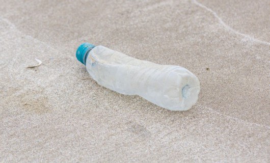 An empty, squashed plastic bottle lies abandoned on a sandy beach.