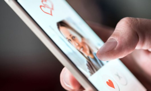 A smartphone shows a dating app, with 'heart' and 'cross' buttons below a smiling girl's picture.