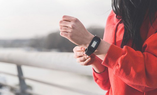 A woman in a red hooded jumper wearing a a black FitBit on her wrist.