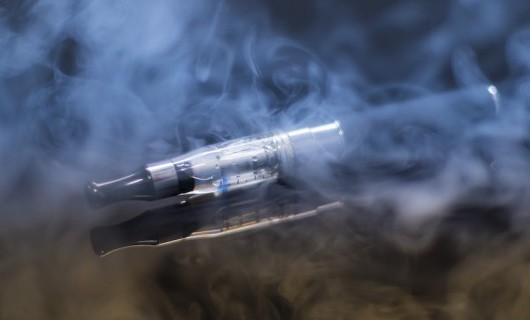A black e-cigarette is visible through a cloud of vapour.