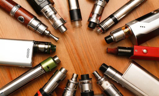 Aerial view of a range of e-cigarettes, arranged in a circle on a wooden surface.