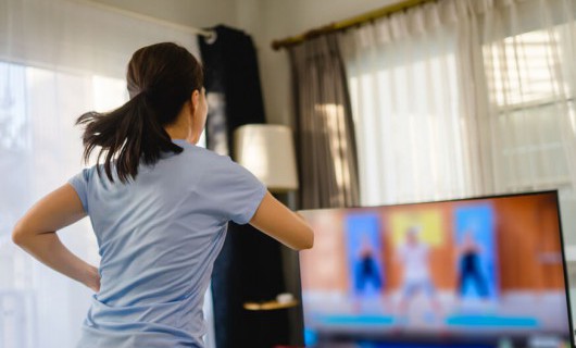A woman is watching a tv screen in her living room, following an exercise routine.
