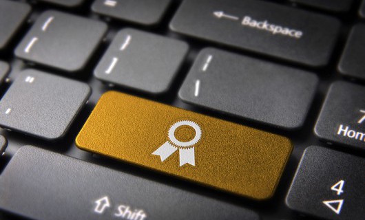 A black computer keyboard with a gold button, showing the image of a rosette.