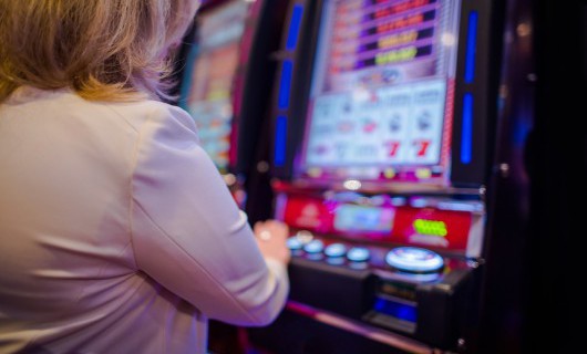 A woman stands next to an arcade slot machine, pressing buttons.
