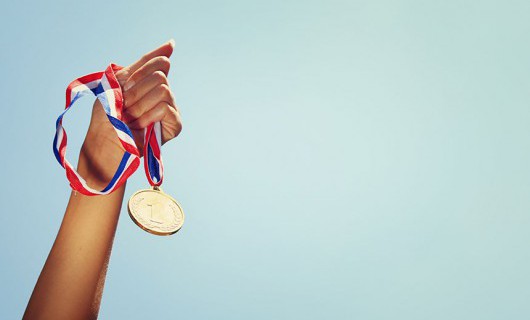 A hand against a blue sky, holding a first place medal.