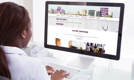 A woman is sat at a computer using the Just Be Croydon website.