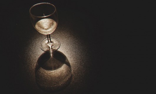 A dark image with a spotlight on a small glass of wine.