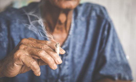 An elderly person's hand is pictured holding a lit cigarette.