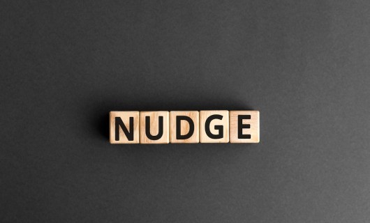 Wooden blocks with letters on them spelling 'NUDGE' against a grey backdrop.